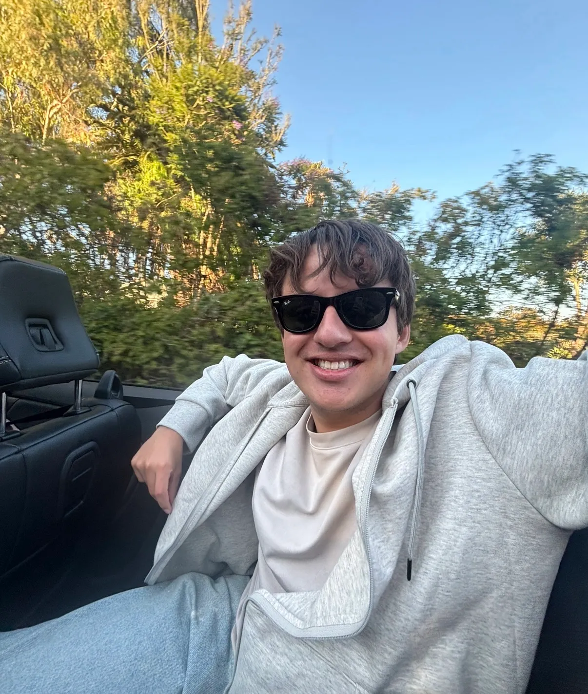 Mateo smiling in sunglasses, riding in a convertible with the top down on a sunny day