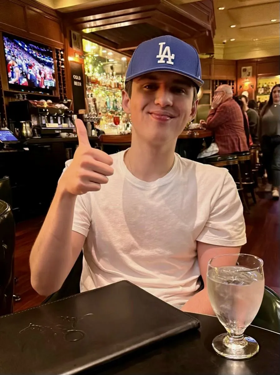 Mateo in a blue LA cap giving a thumbs up at a restaurant table